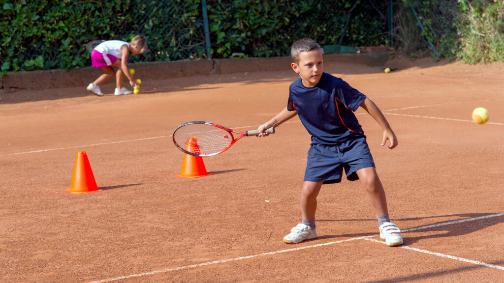 Barn spelar tennis på en grusbana.